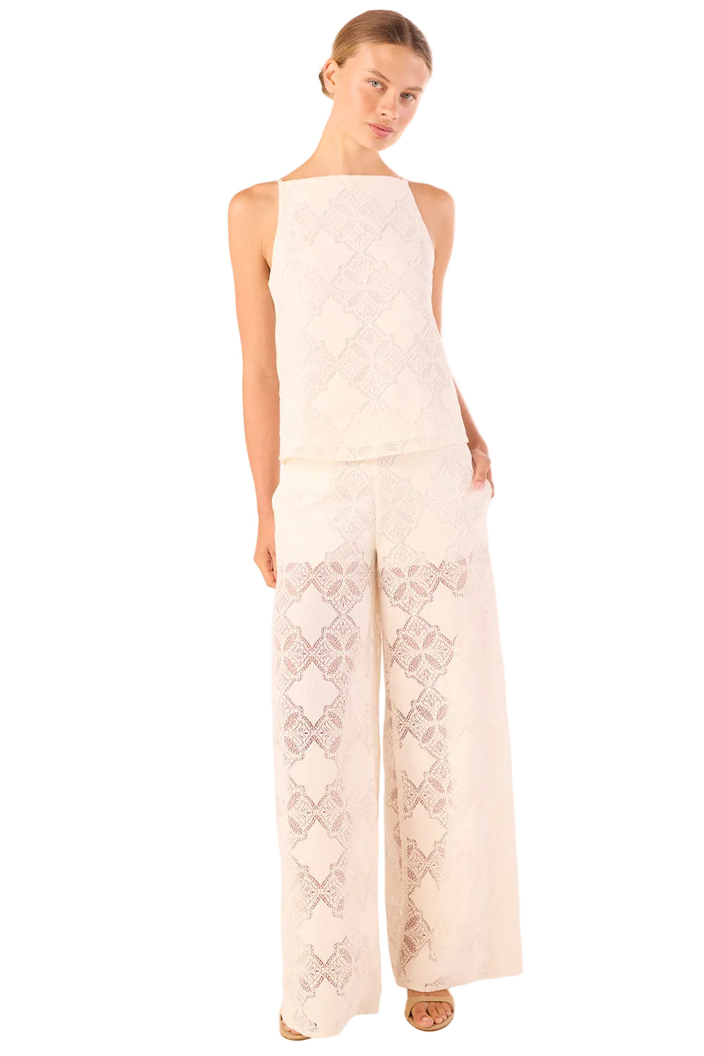 Woman wearing a white sleeveless top and pants with intricate patterns on a light pink background